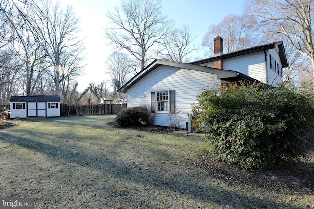 view of property exterior with an outbuilding, fence, a shed, a yard, and a chimney