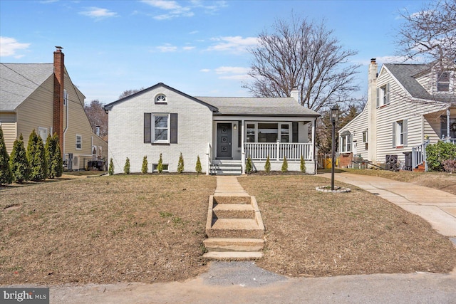 bungalow-style home with brick siding, a porch, a chimney, and a front yard