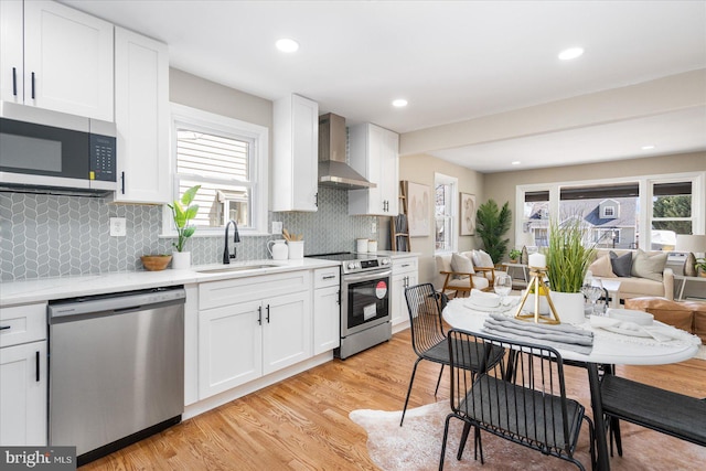 kitchen with light wood-style flooring, a sink, light countertops, appliances with stainless steel finishes, and wall chimney range hood