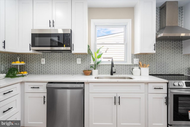 kitchen with a sink, decorative backsplash, appliances with stainless steel finishes, white cabinetry, and wall chimney exhaust hood