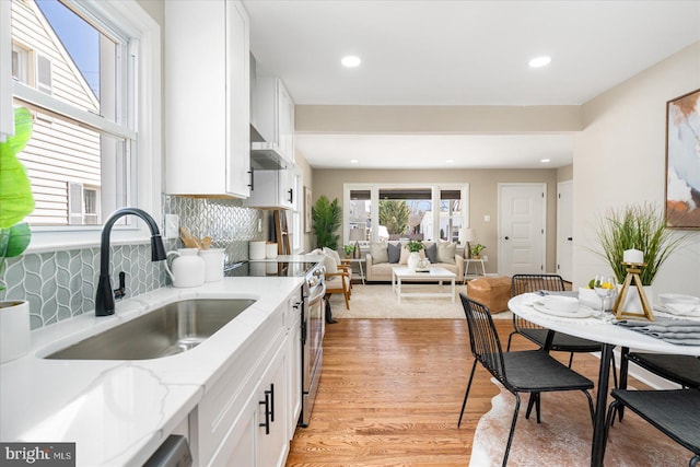 kitchen featuring ventilation hood, light wood finished floors, stainless steel electric stove, a sink, and white cabinetry