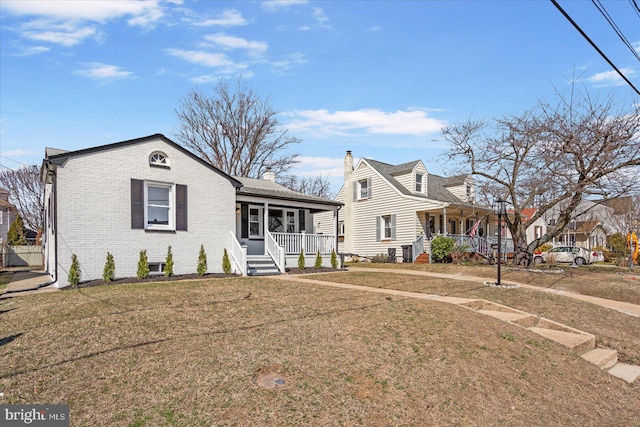 view of front of home featuring brick siding, covered porch, a chimney, and a front yard