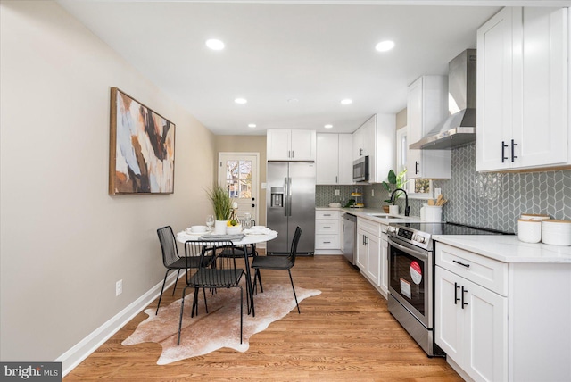 kitchen with light wood-style flooring, appliances with stainless steel finishes, wall chimney range hood, and a sink