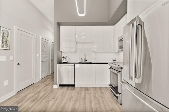 kitchen featuring tasteful backsplash, light wood-type flooring, stainless steel appliances, white cabinetry, and a sink