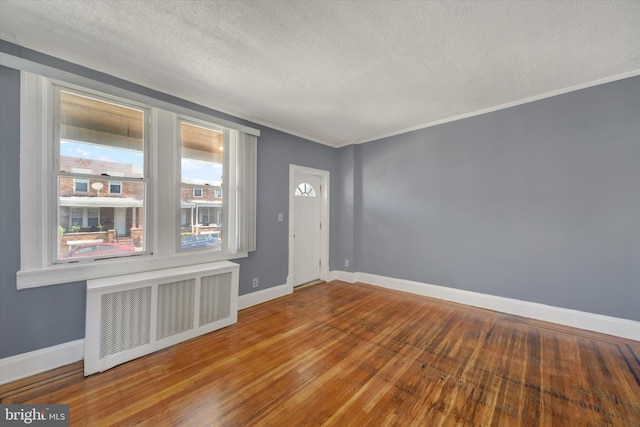 empty room featuring radiator, a textured ceiling, baseboards, and wood-type flooring