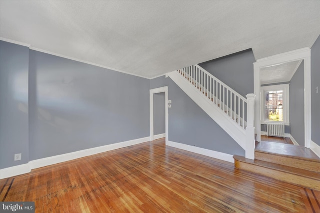 unfurnished living room with crown molding, baseboards, stairs, radiator heating unit, and wood-type flooring