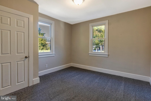 spare room featuring a wealth of natural light, baseboards, and dark carpet