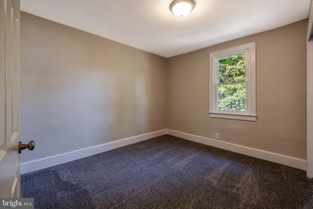 spare room with baseboards and dark carpet