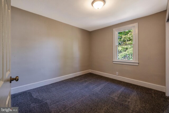 unfurnished room featuring baseboards and dark colored carpet