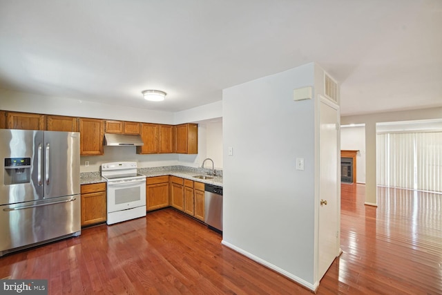 kitchen featuring under cabinet range hood, appliances with stainless steel finishes, dark wood-type flooring, and a sink