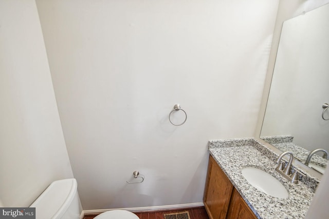 bathroom with vanity, wood finished floors, visible vents, baseboards, and toilet