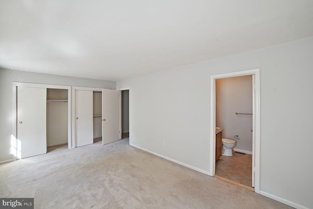 unfurnished bedroom featuring baseboards, light colored carpet, multiple closets, and connected bathroom