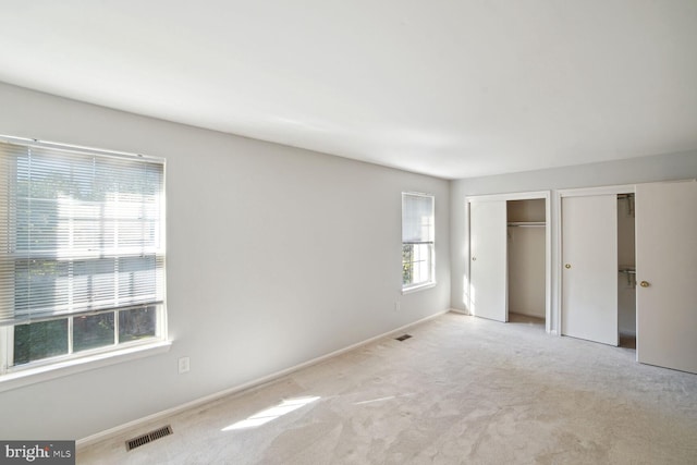 unfurnished bedroom featuring visible vents, carpet flooring, baseboards, and multiple closets