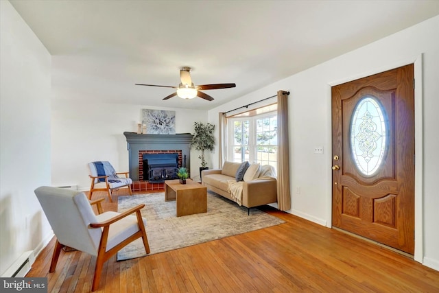 entryway featuring baseboards, ceiling fan, light wood-style floors, a baseboard heating unit, and a brick fireplace