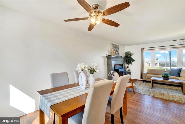 dining room with a fireplace, a ceiling fan, and wood finished floors