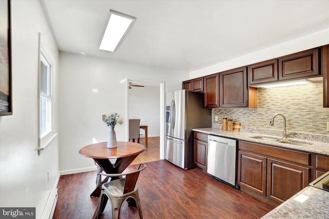 kitchen with light stone counters, a sink, stainless steel appliances, dark wood-type flooring, and tasteful backsplash