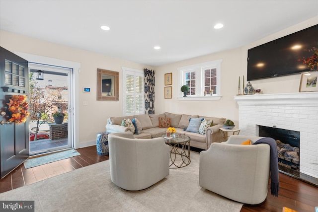 living area featuring recessed lighting, baseboards, a brick fireplace, and wood finished floors