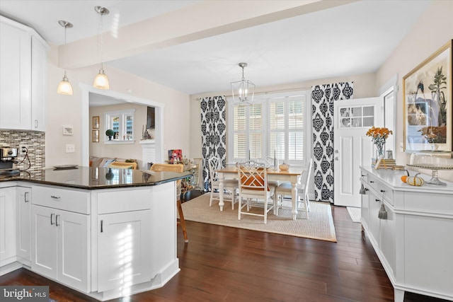 kitchen with dark wood-style floors, white cabinetry, dark countertops, decorative light fixtures, and tasteful backsplash