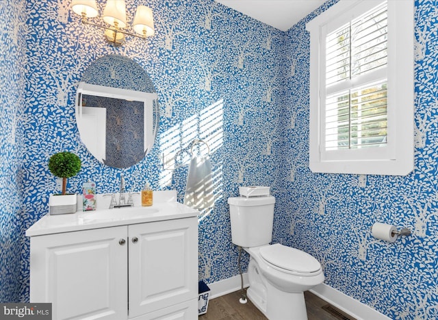 half bathroom with vanity, wood finished floors, baseboards, visible vents, and toilet