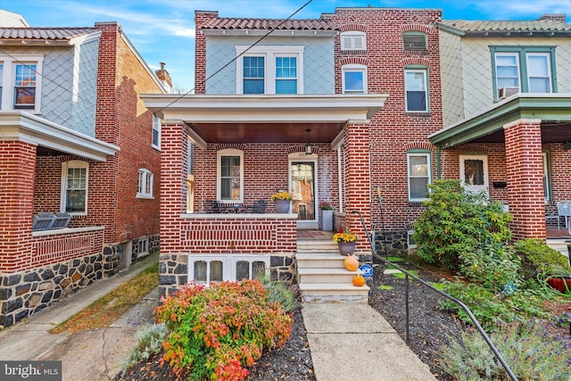 view of front of home with brick siding, a porch, and a tiled roof