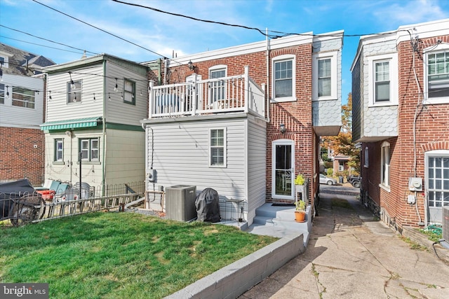 rear view of property featuring fence, a lawn, brick siding, and central AC