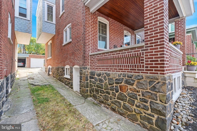 view of home's exterior with a detached garage, stone siding, brick siding, and an outdoor structure