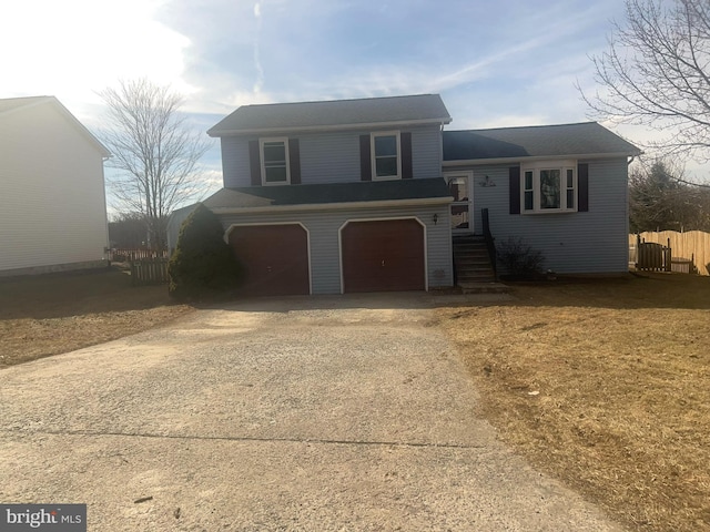 split level home featuring an attached garage, concrete driveway, and fence