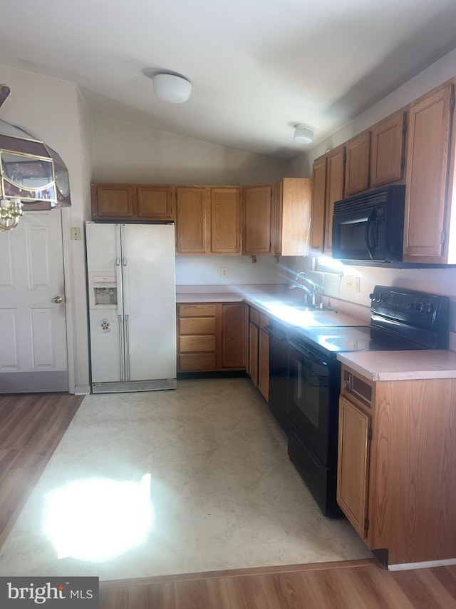 kitchen featuring black appliances, a sink, light wood finished floors, lofted ceiling, and light countertops