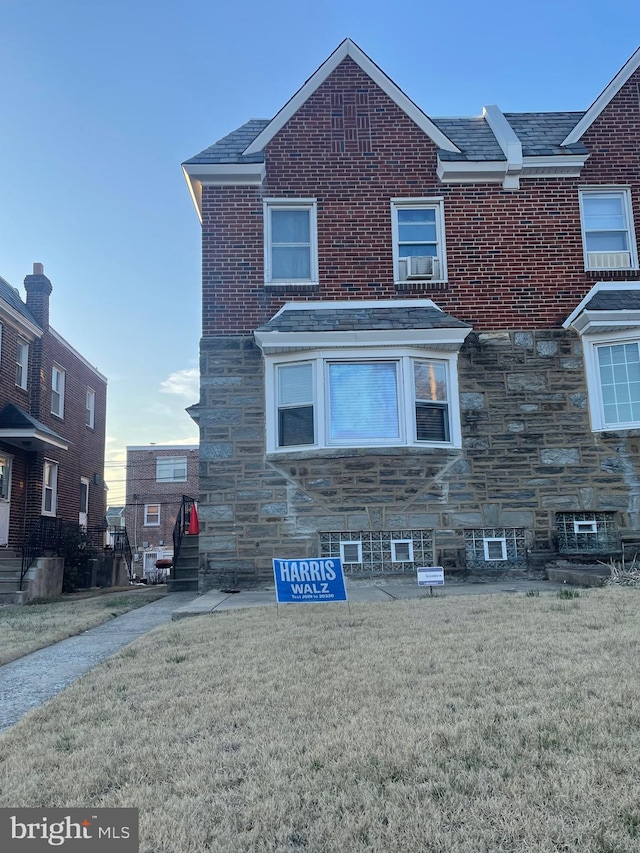 view of front of house with brick siding, stone siding, cooling unit, and a front yard