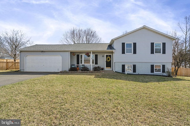 tri-level home with aphalt driveway, fence, a garage, and a front yard