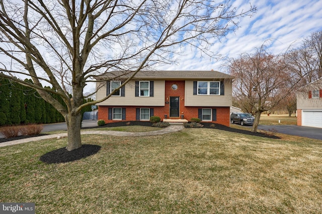 raised ranch with aphalt driveway, brick siding, and a front lawn