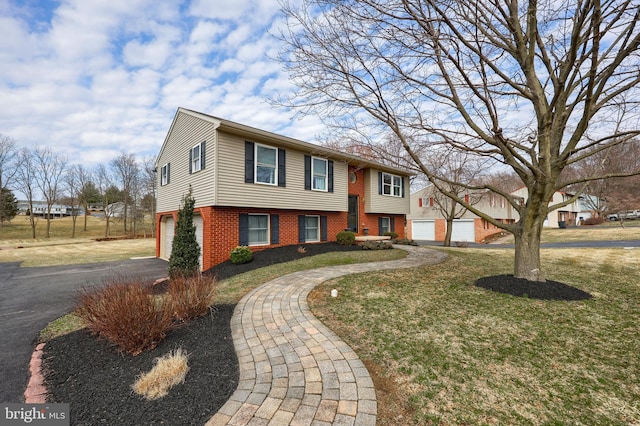 bi-level home with aphalt driveway, a garage, brick siding, and a front yard