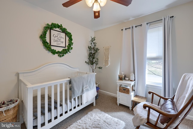 carpeted bedroom featuring baseboards, a crib, and a ceiling fan