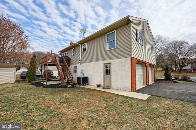 back of house with aphalt driveway, stairway, central air condition unit, a yard, and a garage