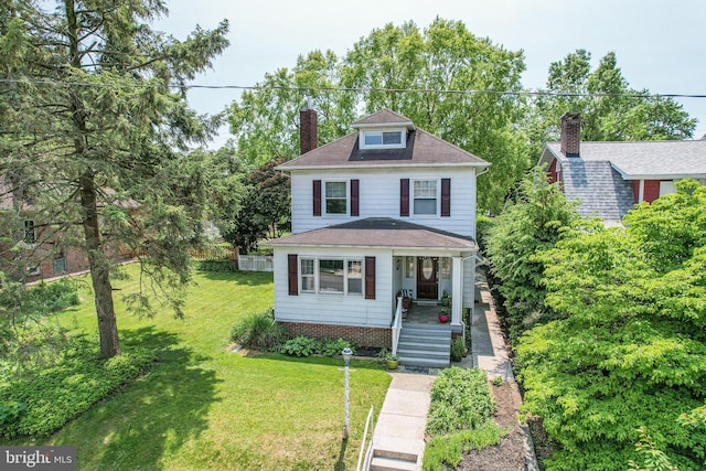 american foursquare style home with covered porch, a chimney, a front yard, and roof with shingles