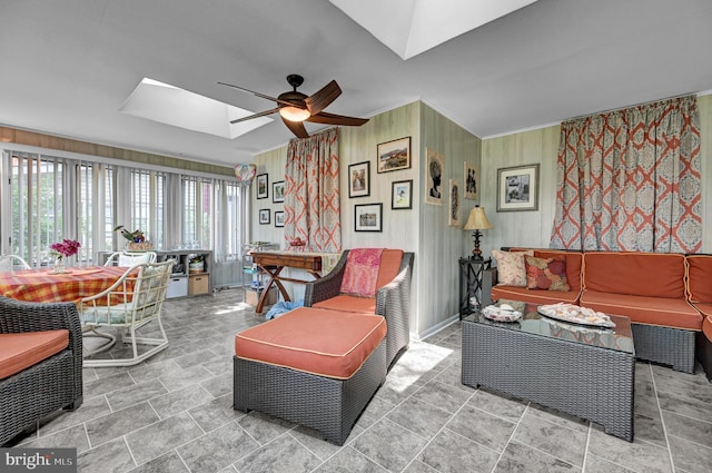 living room with baseboards, a skylight, ornamental molding, ceiling fan, and stone finish flooring