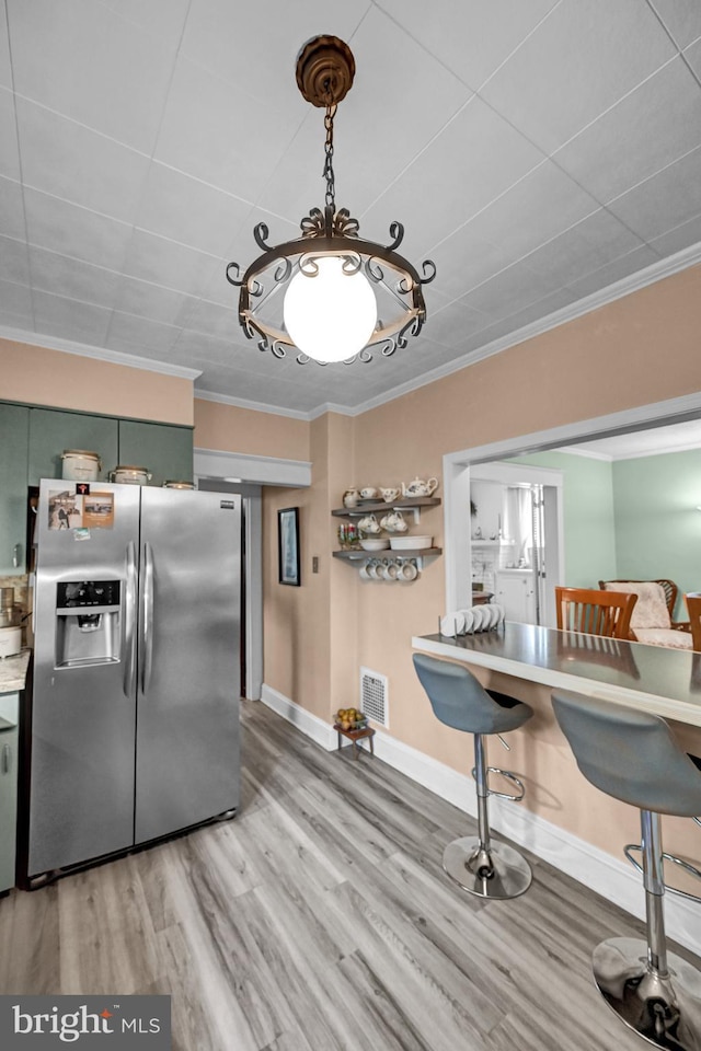 kitchen with visible vents, ornamental molding, light wood-style flooring, stainless steel fridge, and green cabinetry