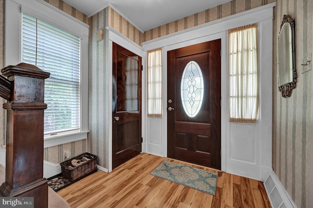 foyer featuring visible vents, wallpapered walls, baseboards, and wood finished floors