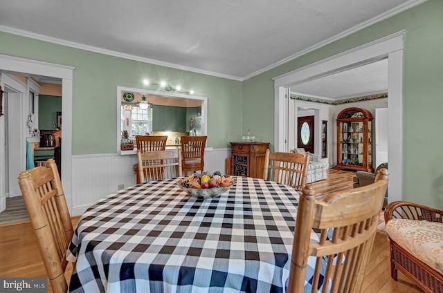 dining space featuring ornamental molding, light wood-style floors, and wainscoting