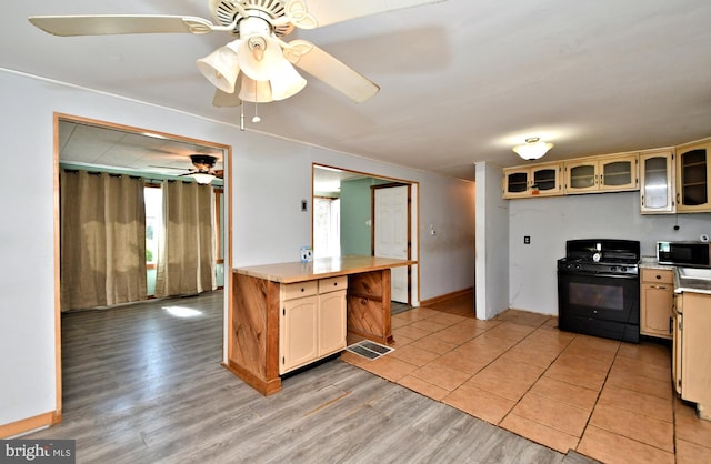 kitchen featuring black gas range, light wood-style floors, light countertops, glass insert cabinets, and ceiling fan