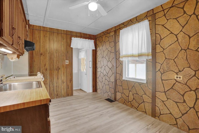 kitchen with a ceiling fan, light wood finished floors, butcher block countertops, a sink, and brown cabinets