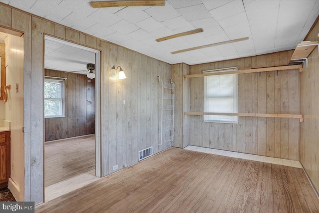 unfurnished room with wood finished floors, visible vents, wood walls, and ceiling fan