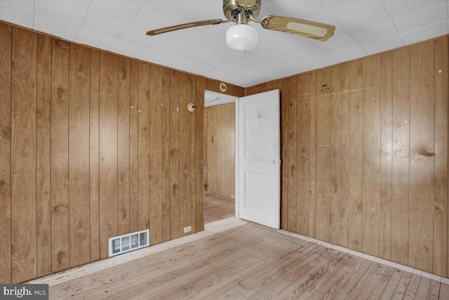 unfurnished room with visible vents, wood walls, and wood finished floors