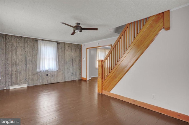 unfurnished living room with stairs, hardwood / wood-style flooring, a ceiling fan, and baseboards