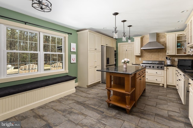 kitchen with stone tile floors, appliances with stainless steel finishes, cream cabinets, wall chimney exhaust hood, and open shelves