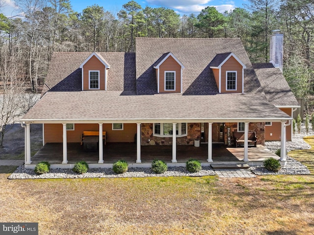 view of front of home with stone siding, a porch, a front yard, and roof with shingles