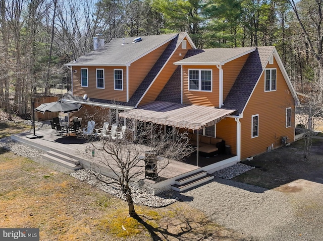 rear view of house featuring a wooden deck, outdoor dining area, a chimney, and a shingled roof