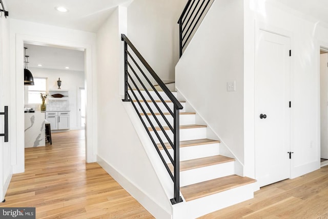 staircase with recessed lighting, a barn door, baseboards, and wood finished floors