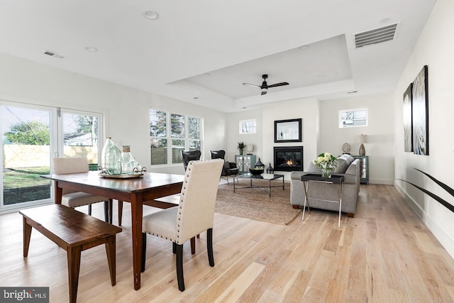 dining area with a glass covered fireplace, a raised ceiling, visible vents, and light wood finished floors