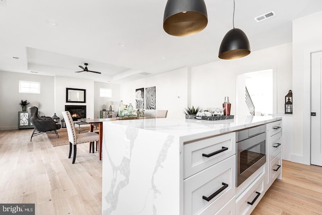 kitchen featuring stainless steel microwave, a raised ceiling, visible vents, and a glass covered fireplace